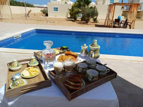 een dienblad met eten op een tafel naast een zwembad bij DAR EL JERBIA in Midoun