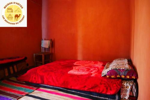 un letto rosso in un angolo di una stanza di maison d'hôtes les Bédouins du désèrt a Foum Zguid
