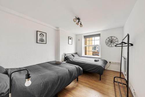 ロンドンにあるSleek Shoreditch Hideout - 2 Bed Gem with Balcony in Central Londonのベッドルーム1室(ベッド2台、壁掛け時計付)