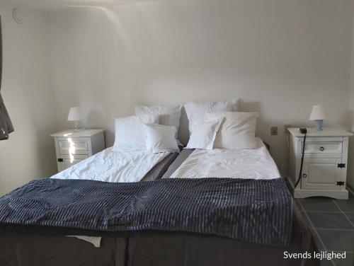 uma cama com lençóis e almofadas brancos e duas mesas de cabeceira em Døssinghus Holiday Apartments em Kjellerup