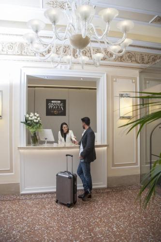 a man with a suitcase and a woman at a counter at Hotel Grande Italia in Chioggia