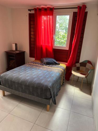 a bedroom with a bed and a window with red curtains at Kama in Sainte-Luce