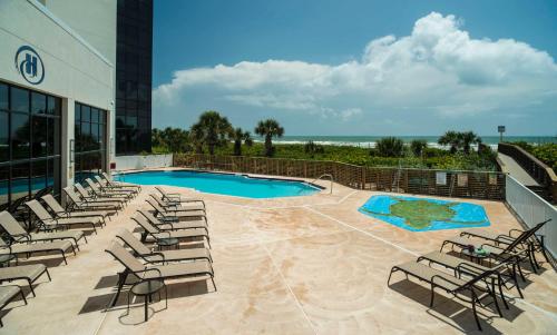 a swimming pool with lounge chairs next to a building at Hilton Cocoa Beach Oceanfront in Cocoa Beach