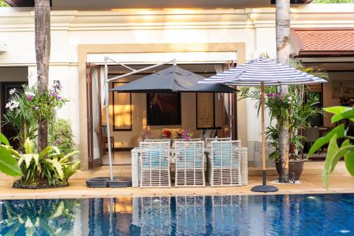 two umbrellas and chairs next to a swimming pool at Saitaan Villa Dennapa Bang Tao Beach in Bang Tao Beach