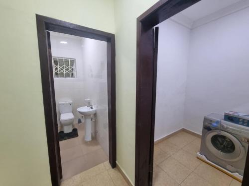 a bathroom with a toilet and a washing machine at B's Classic and Cozy Apartments in Cape Coast