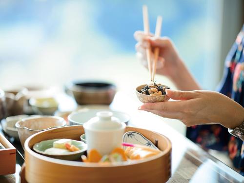 a person holding a bowl of food with chopsticks at Shima Kanko Hotel The Bay Suites in Shima
