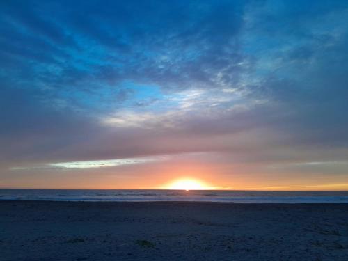 a sunset on a beach with the sun in the distance at Tres Velas Surf in Celestino Gasca