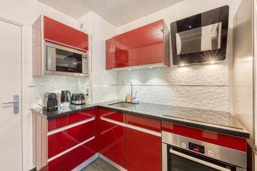 une cuisine avec des armoires rouges et un micro-ondes dans l'établissement Ô COCON DE FRANCONVILLE - LOGEMENT AVEC GRANDE TERRASSE - 24H ACCESS, à Franconville