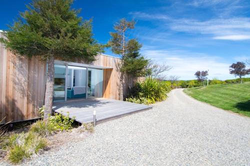 a house on a gravel road next to a tree at Kina Retreat - Luxury Nelson Getaway in Tasman