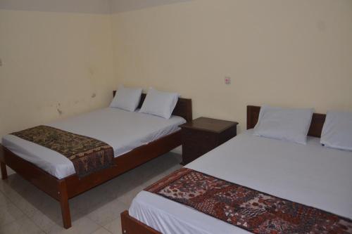 a room with two beds with white sheets at OYO 93736 Homestay Joglo Dephis Syariah in Magelang