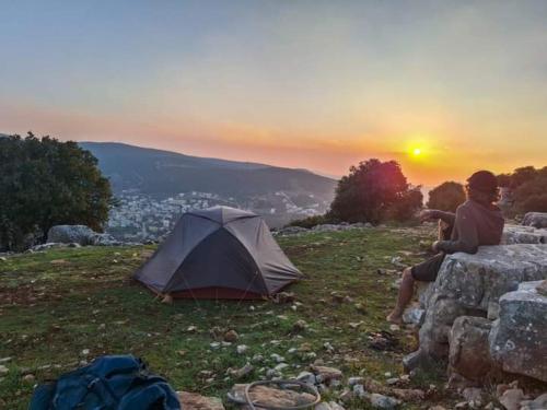 a person sitting on a rock next to a tent at - Trekking from Dana to Petra in Dana