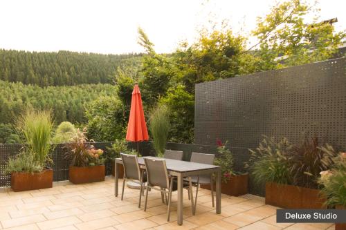 eine Terrasse mit einem Tisch, Stühlen und einem roten Regenschirm in der Unterkunft Rurtal de luxe in Simmerath