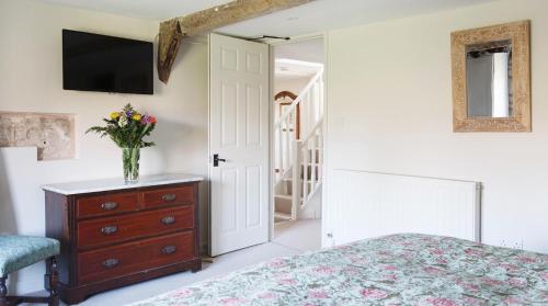 a bedroom with a bed and a vase of flowers on a dresser at A handsome large 9 bedroom 17th Century village house moments from The Cotswold Way offering modern luxury in a peaceful location in Frocester