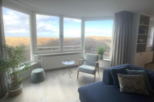 a living room with a blue couch and a large window at Zeewaarts in Cadzand