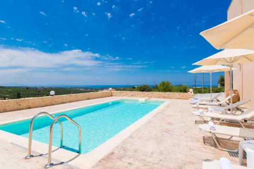 a swimming pool with chairs and umbrellas next to a building at Domas Blue Studio Villa With Private Pool and Panoramic View in Loutra