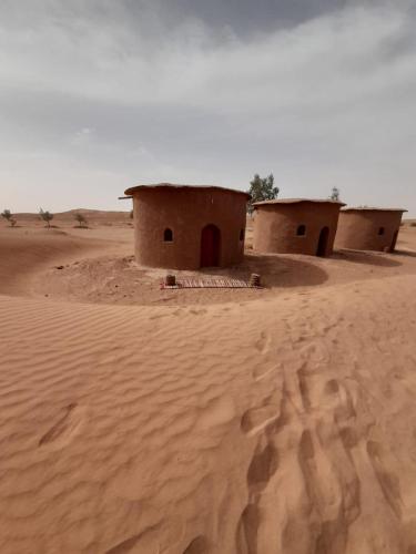 two houses in the desert with footprints in the sand at Camp Iguidi Tours in Mhamid