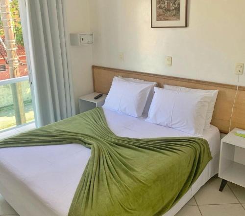 a bedroom with a bed with a green blanket on it at Hotel Palmar in Guarujá