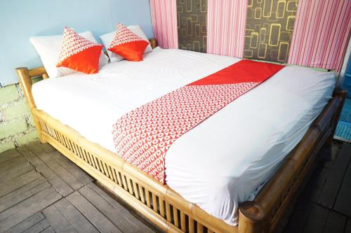una cama de madera con almohadas rojas y blancas. en Collection O 93000 Karona Berg Homestay & Cafe, en Banyuwangi