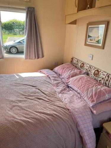 a bed with pink sheets in a room with a window at Caravan in Mablethorpe