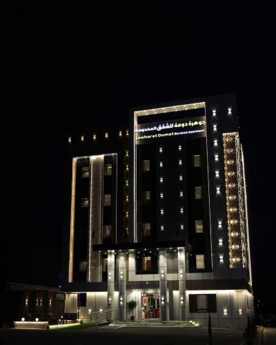 a tall building with lights on it at night at جوهرة دومة الجندل للشقق المخدومة Jawharat Dumat Serviced Apartments in Dawmat al Jandal