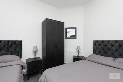 a bedroom with two beds and a black cabinet at Lovely 2-Bedroom Bungalow Sleeps 6 with Garden and Off Road Parking by Amazing Spaces Relocations Ltd in Crank