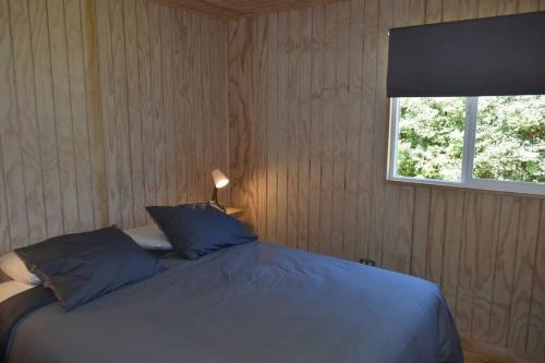 a bedroom with a bed with blue pillows and a window at Beautiful Don Pedro Cabin, Chilean Patagonia. in Chaitén