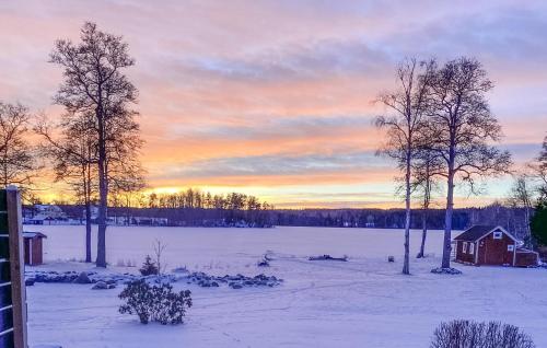 a snowy field with a house and trees in the sunset at Lovely Home In Ormaryd With Sauna in Ormaryd