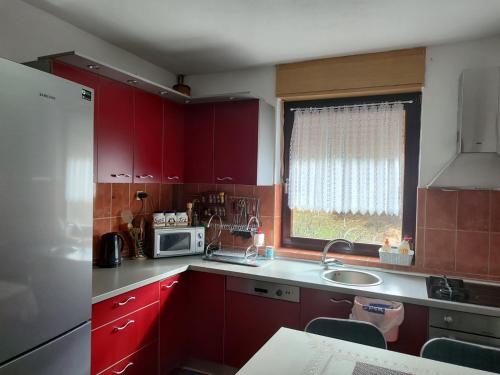 a kitchen with red cabinets and a sink and a window at Villa Artemida apartman in Kulen Vakuf