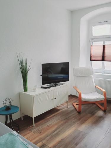 a living room with a tv and a white chair at Terrassenwohnung Nordlicht in Grimma