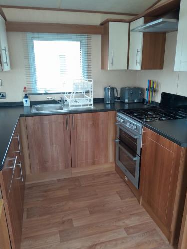 a kitchen with wooden cabinets and a stove top oven at Sunnymeade Holiday Park i3 St David in Ingoldmells