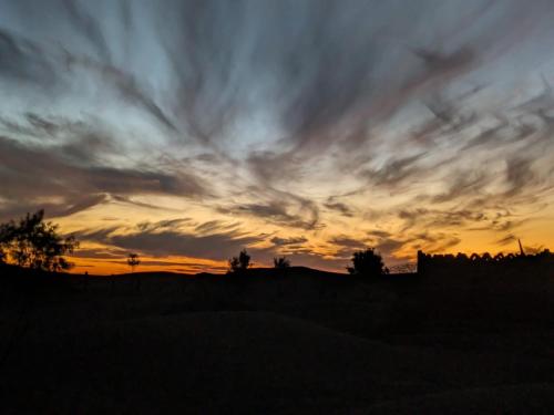 a sunset over a field with a fence at Camp Iguidi Tours in Mhamid