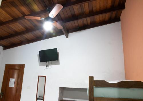 Habitación con ventilador de techo y TV en la pared. en Recanto da Rose Guesthouse, en Caraguatatuba