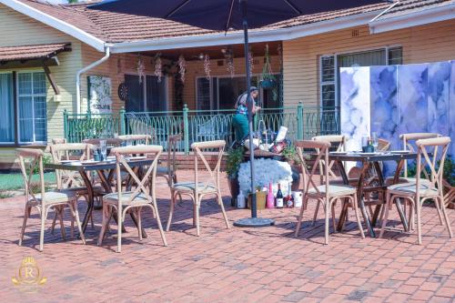 a woman sitting at tables and chairs under an umbrella at Royal Highness Lux Guesthouse in Carletonville