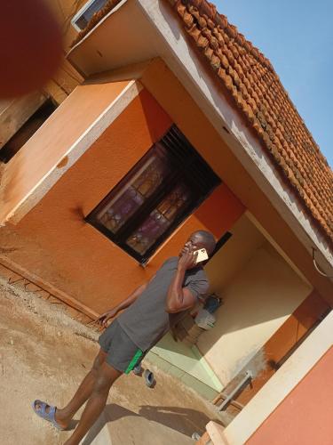 Ein Mann steht vor einem Haus und redet mit einem Handy. in der Unterkunft foxxies guest house in Buloba