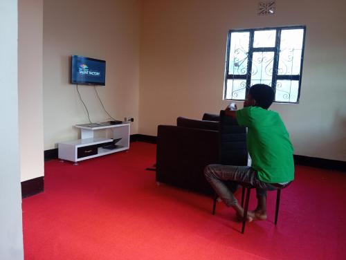 un homme assis sur une chaise et regardant la télévision dans l'établissement Kilimanjaro Homestay, à Boma la Ngombe