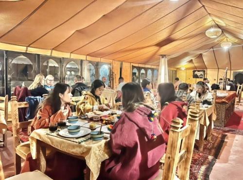 un grupo de personas sentadas en mesas en una tienda en Desert Coast Opulent Camp, en Merzouga