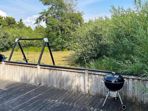 un grill assis sur une terrasse en bois à côté d'une clôture dans l'établissement 4 person holiday home in R m, à Lakolk