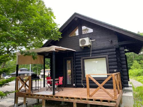 a black cabin with a deck and a table and chairs at 真狩村焚き火キャンプ場 in Makkari