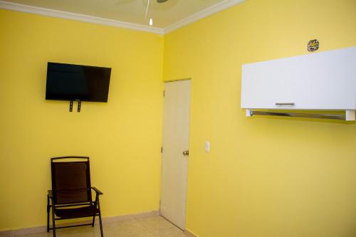 a room with a yellow wall with a tv and a chair at Comfort House in Santa Marta