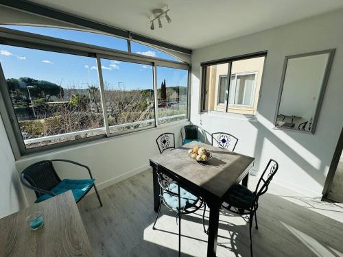 une salle à manger avec une table, des chaises et des fenêtres dans l'établissement Bel appartement refait à neuf, au calme avec parking privatif à Agde - FR-1-723-131, au Cap d'Agde