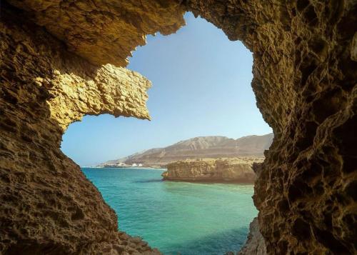 a view of the ocean through a rock window at Wadi shab chalet in Ţīwī