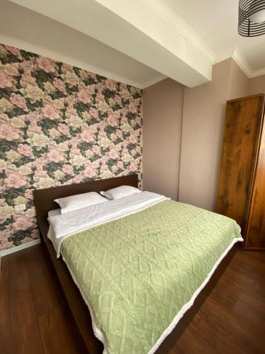 una camera con un letto verde con una parete floreale di ЖК Весна a Almaty