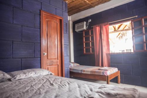a bedroom with a blue wall with a bed and a window at Hostel El Gran Azul Olon in Olón