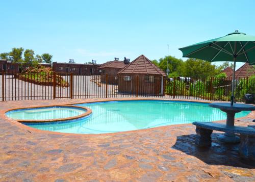 a swimming pool with an umbrella and a bench at Crocodile Pools Resort in Gaborone