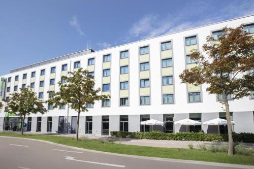 ein großes weißes Gebäude mit Sonnenschirmen davor in der Unterkunft Holiday Inn Express Augsburg, an IHG Hotel in Augsburg