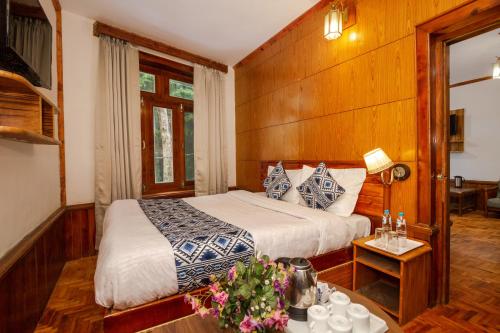 a bedroom with a bed and a table with flowers at Holiday Home International -Vivaan Stays in Manāli