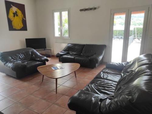 a living room with black leather furniture and a table at Villas de La Ferme Du Gros Noyer in Malaucène