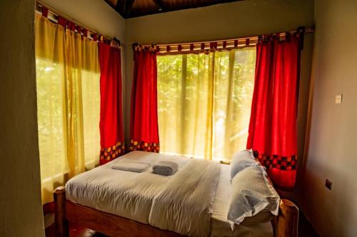 KapchorwaにあるMise cave lodgeの赤いカーテン付きのベッドルーム1室、窓の前にベッド1台が備わります。