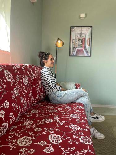 a woman is sitting on a red couch at בין הר ובין ים in Ovnat