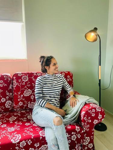 a woman sitting on a red couch next to a lamp at בין הר ובין ים in Ovnat